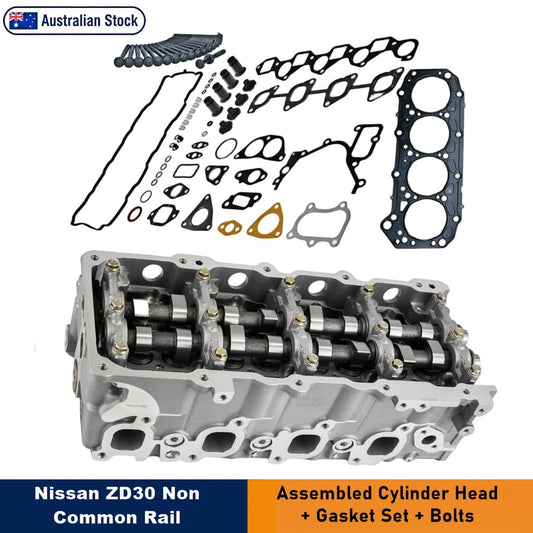 Nissan ZD30 Non-Common Rail Cylinder Head and Gasket Kit. The image features an assembled silver aluminium cylinder head with camshaft barrels, accompanied by a large black gasket. Various black and gold gaskets, seals, and bolts are arranged above the cylinder head on a white background. Text overlays indicate "Nissan ZD30 Non-Common Rail" and "Assembled Cylinder Head + Gasket Set + Bolts."